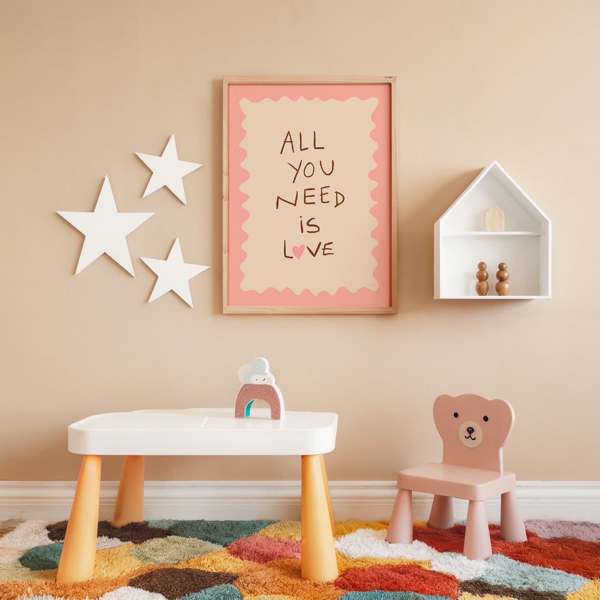 All you need is love lettering nursery print in an oak frame on a peach wall above a kids table with wall stars