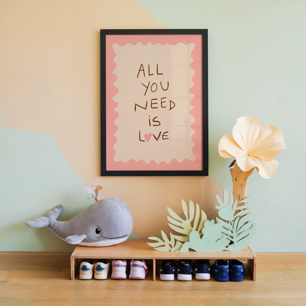 All you need is love lettering nursery print in a black frame on a mint and peach wall above a whale plush