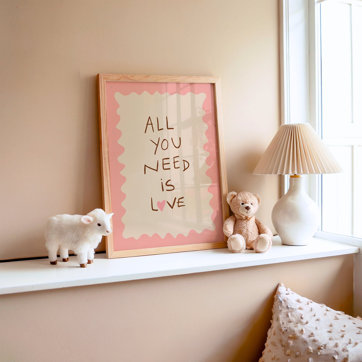 All you need is love lettering nursery print in an oak frame on a window ledge with a toy lamb and teddy