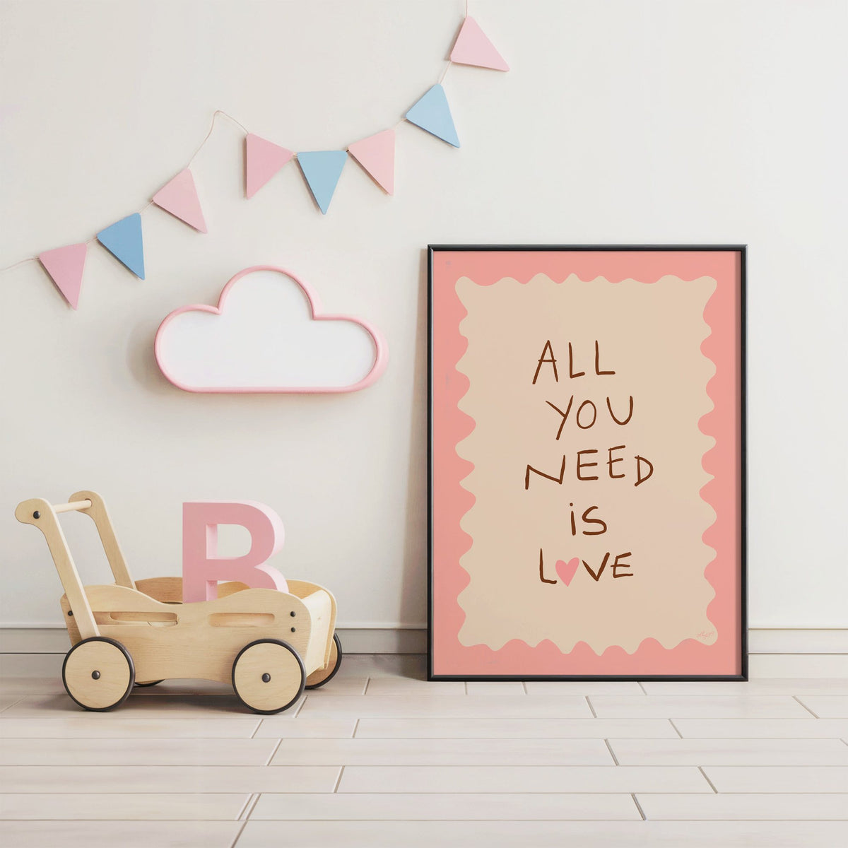 All you need is love lettering nursery print in a black frame under pastel bunting by a wooden baby walker