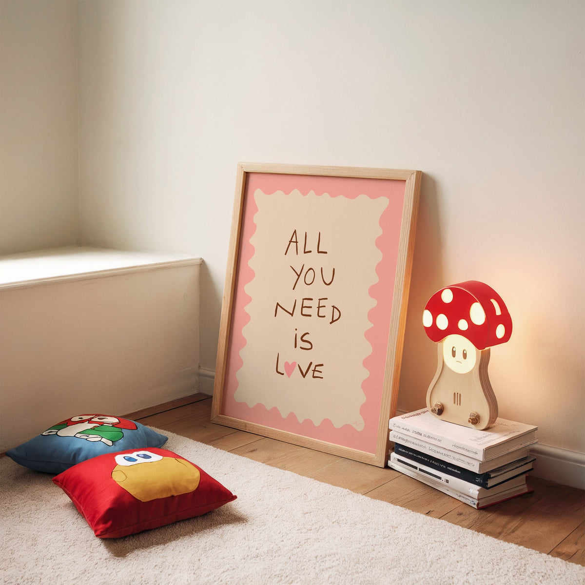 All you need is love lettering nursery print in an oak frame leaning on a rug beside a mushroom lamp and floor cushions