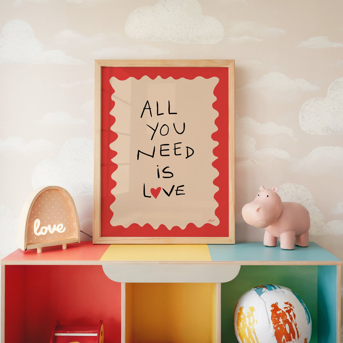 All you need is love heart nursery print in an oak frame on a rainbow toy shelf against cloud wallpaper