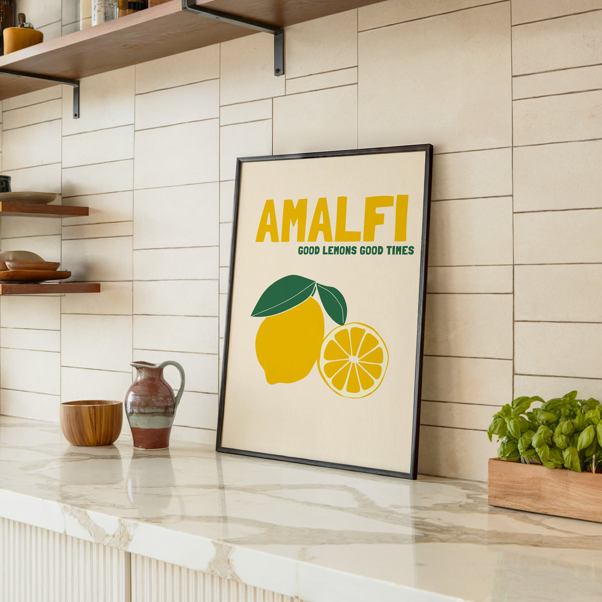 Amalfi lemon print in a black frame leaning on a marble counter in a tiled kitchen