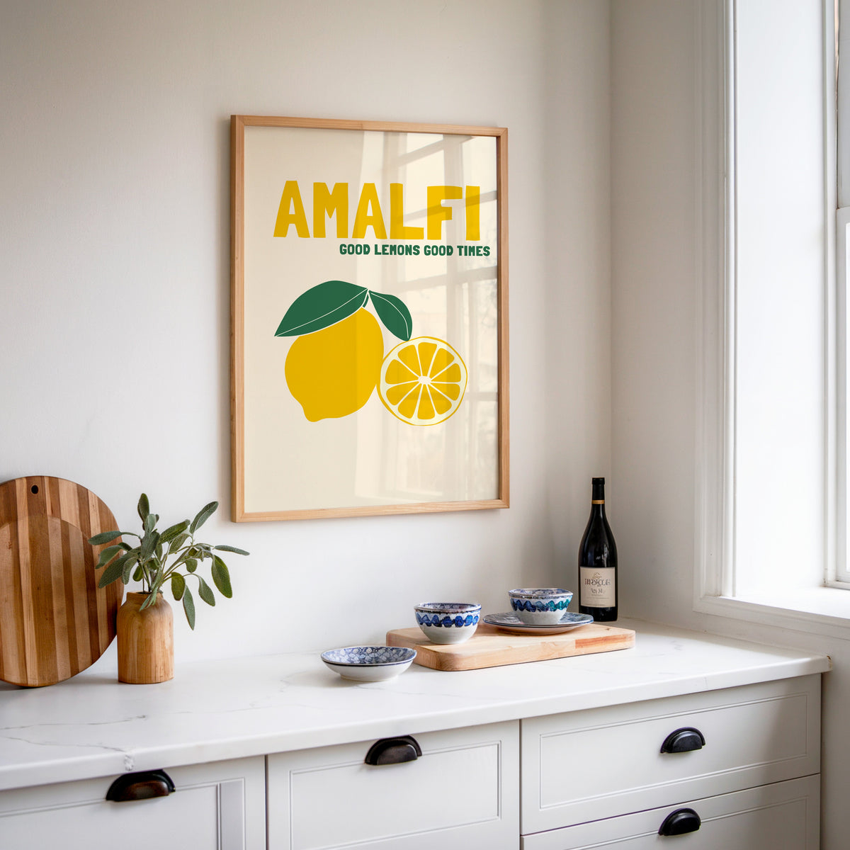 Amalfi lemon print in an oak frame above a white sideboard with a bottle of wine