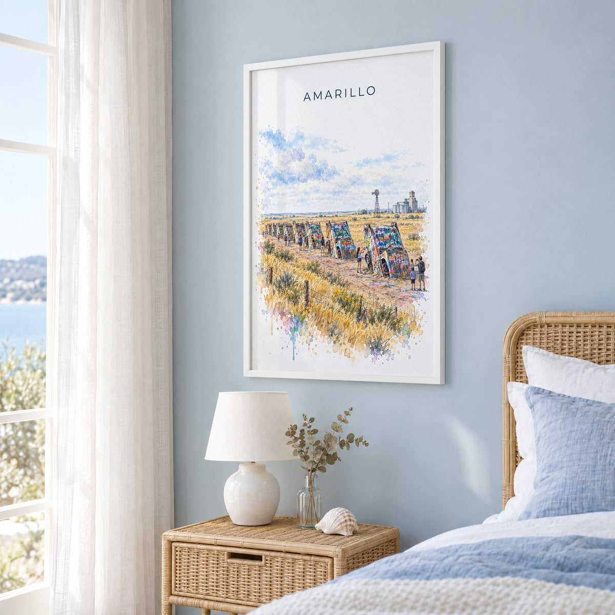 Amarillo watercolor print in a white frame on a pale blue wall beside a rattan bed in a coastal bedroom