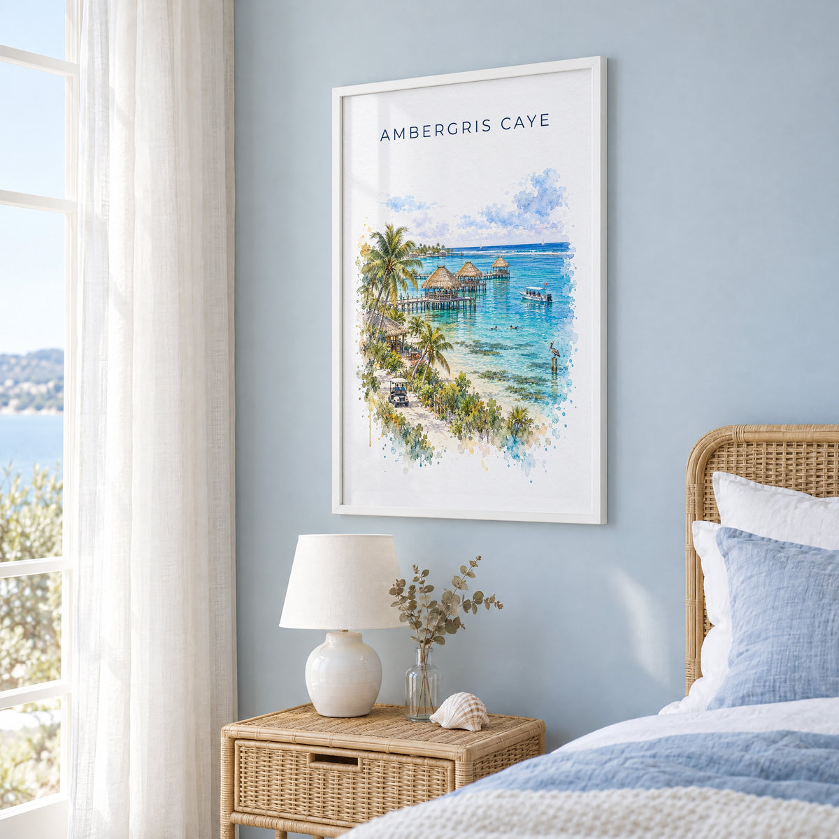 Ambergris Caye watercolor print in a white frame on a pale blue wall beside a rattan bed in a coastal bedroom