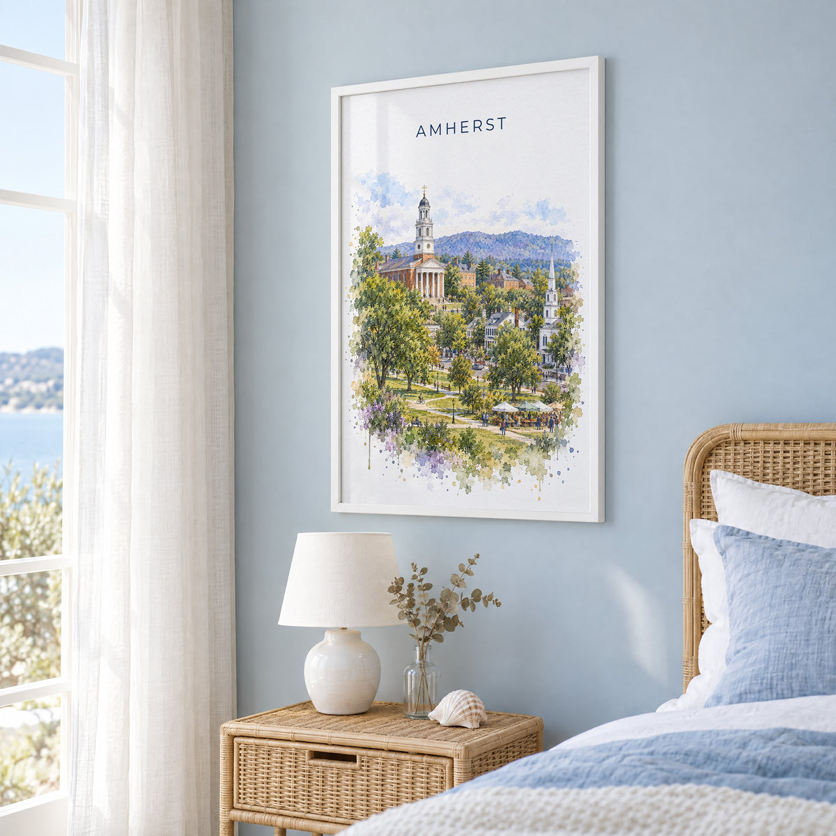 Amherst, Massachusetts watercolor print in a white frame on a pale blue wall beside a rattan bed in a coastal bedroom