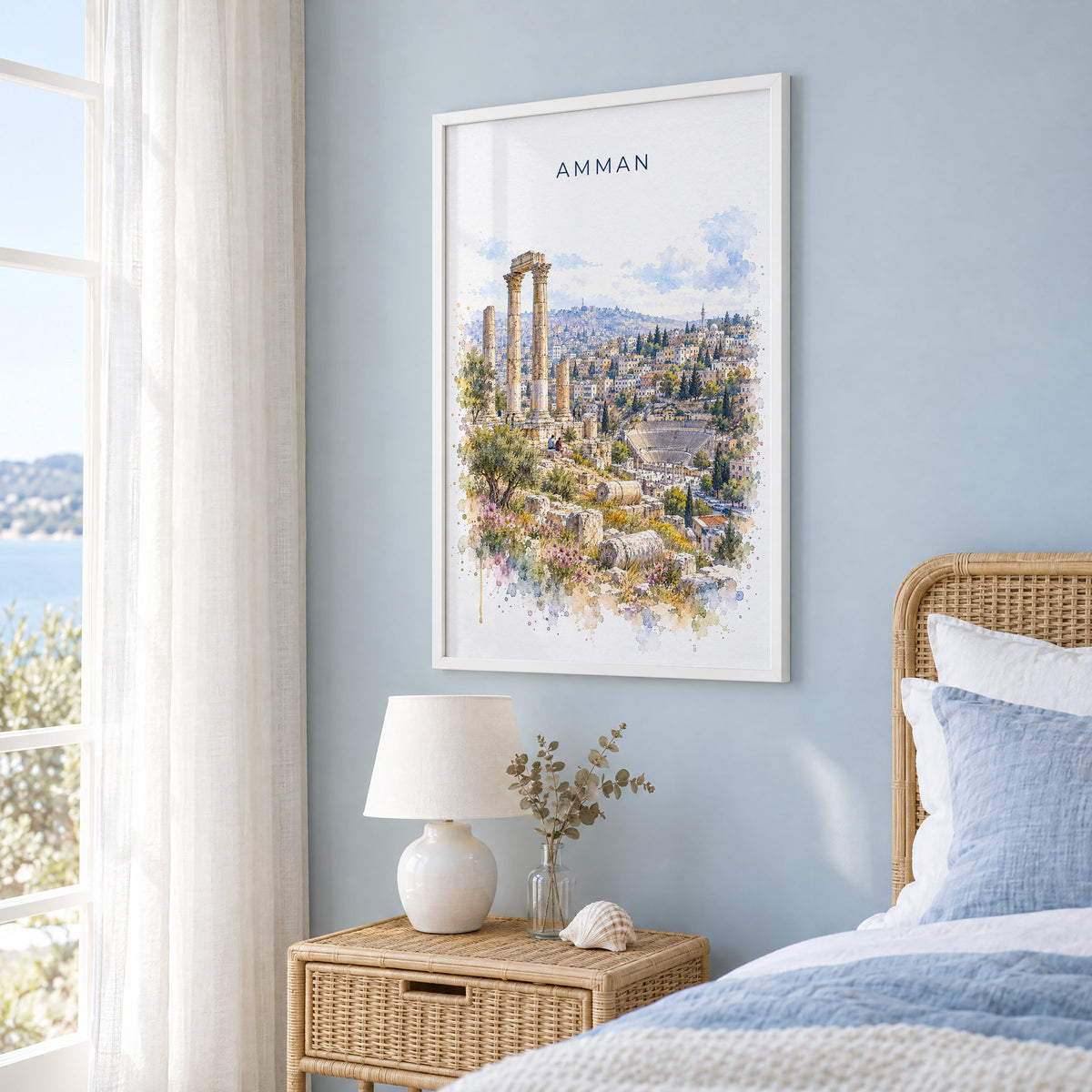 Amman watercolor print in a white frame on a pale blue wall beside a rattan bed in a coastal bedroom