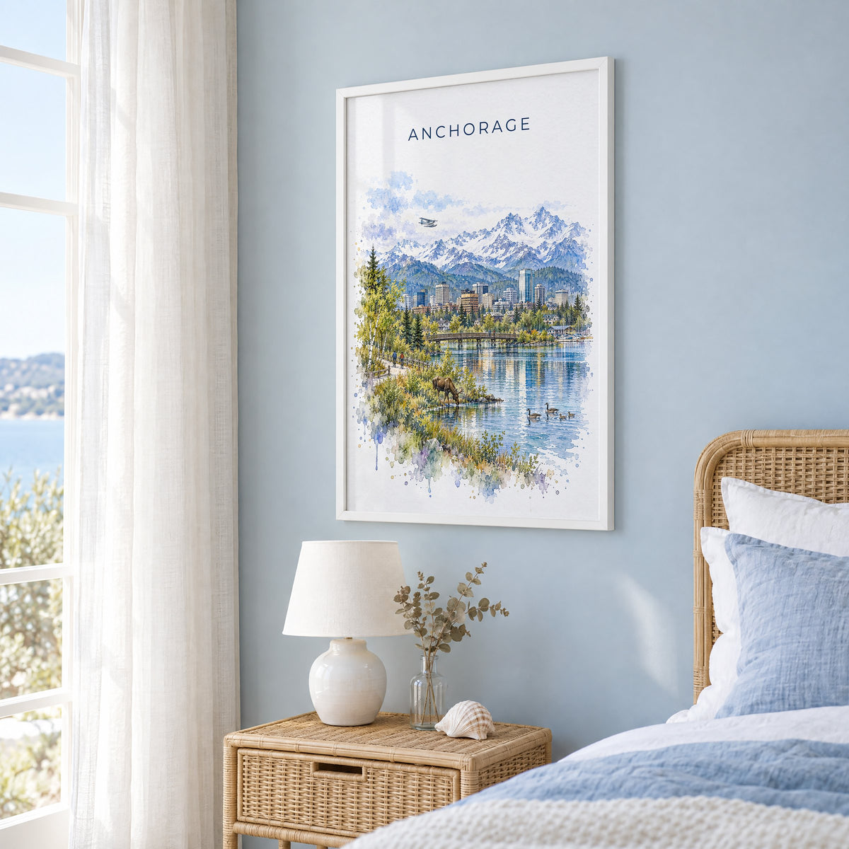 Anchorage watercolor print in a white frame on a pale blue wall beside a rattan bed in a coastal bedroom