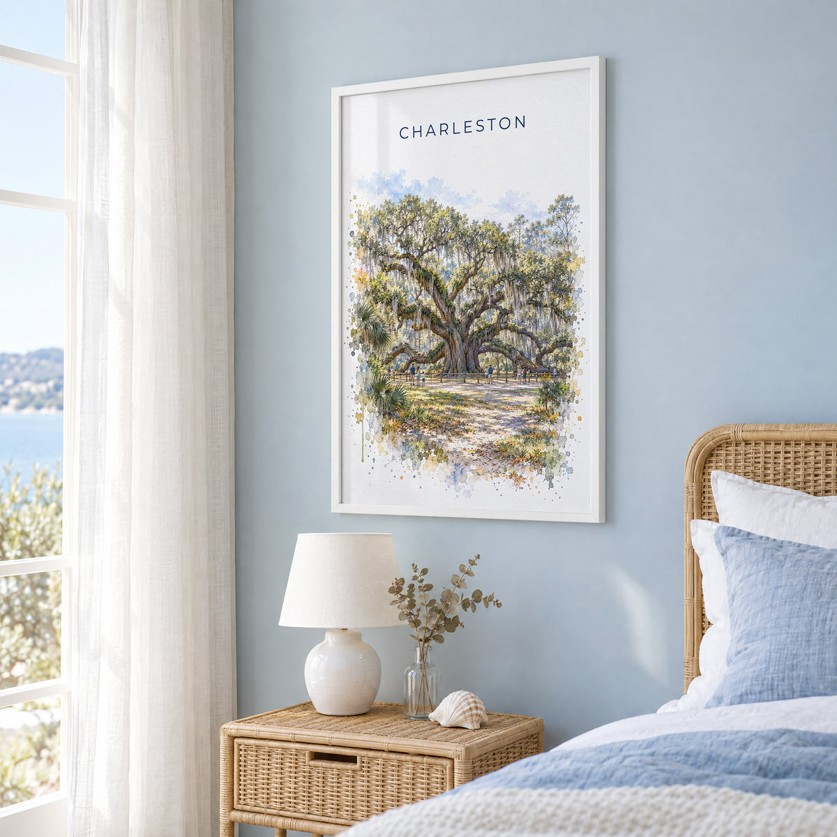 Angel Oak Charleston watercolor print in a white frame on a pale blue wall beside a rattan bed in a coastal bedroom