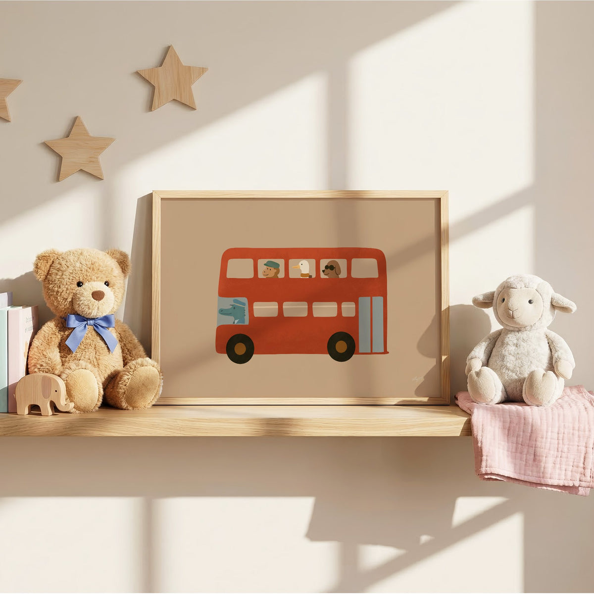 Animals riding red double decker bus nursery print in an oak frame on a wall shelf between a teddy bear and a toy lamb