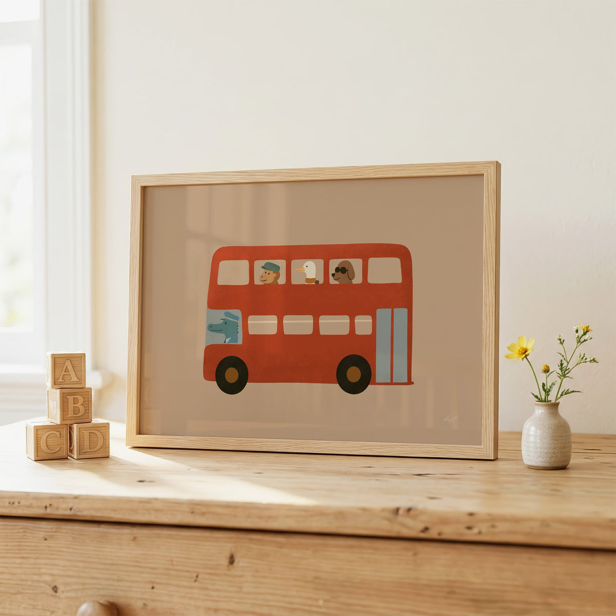 Animals riding red double decker bus nursery print in an oak frame on a wooden dresser beside ABC blocks