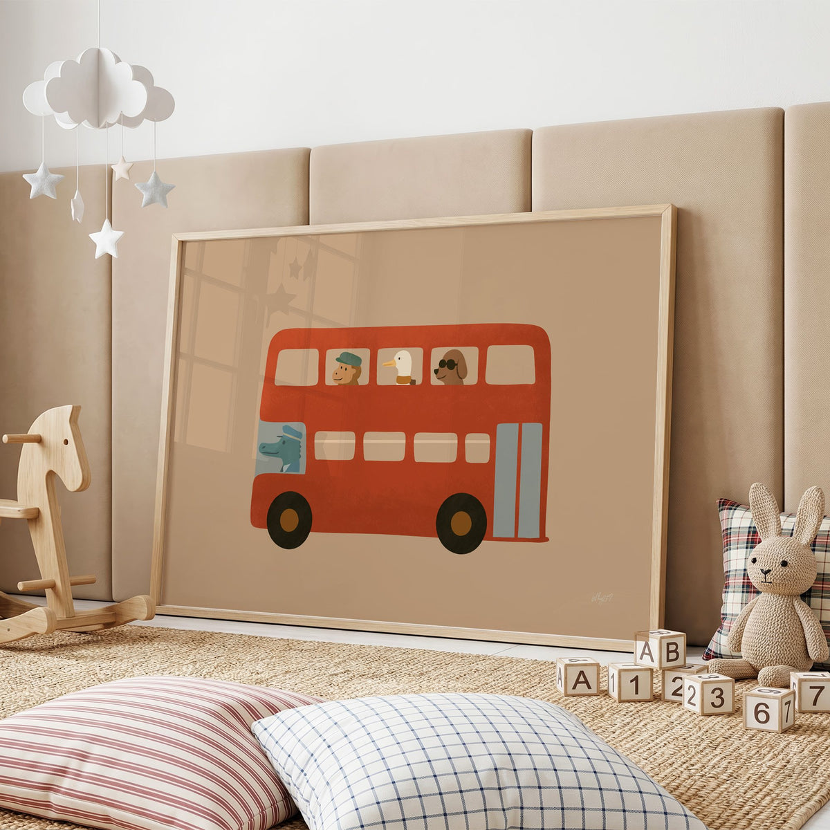Animals riding red double decker bus nursery print in an oak frame on a padded wall by a wooden rocking horse