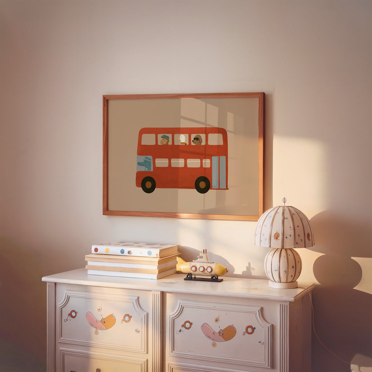 Animals riding red double decker bus nursery print in a cherry wood frame above a painted dresser and lamp