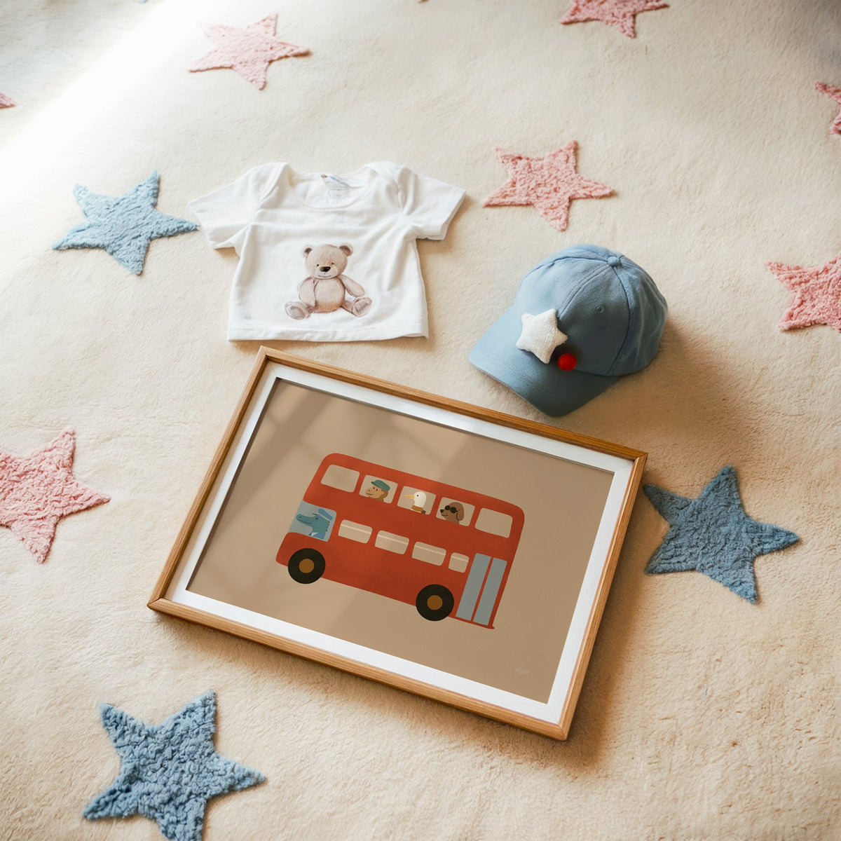 Animals riding red double decker bus nursery print in a matted oak frame on a star rug with a baby tee