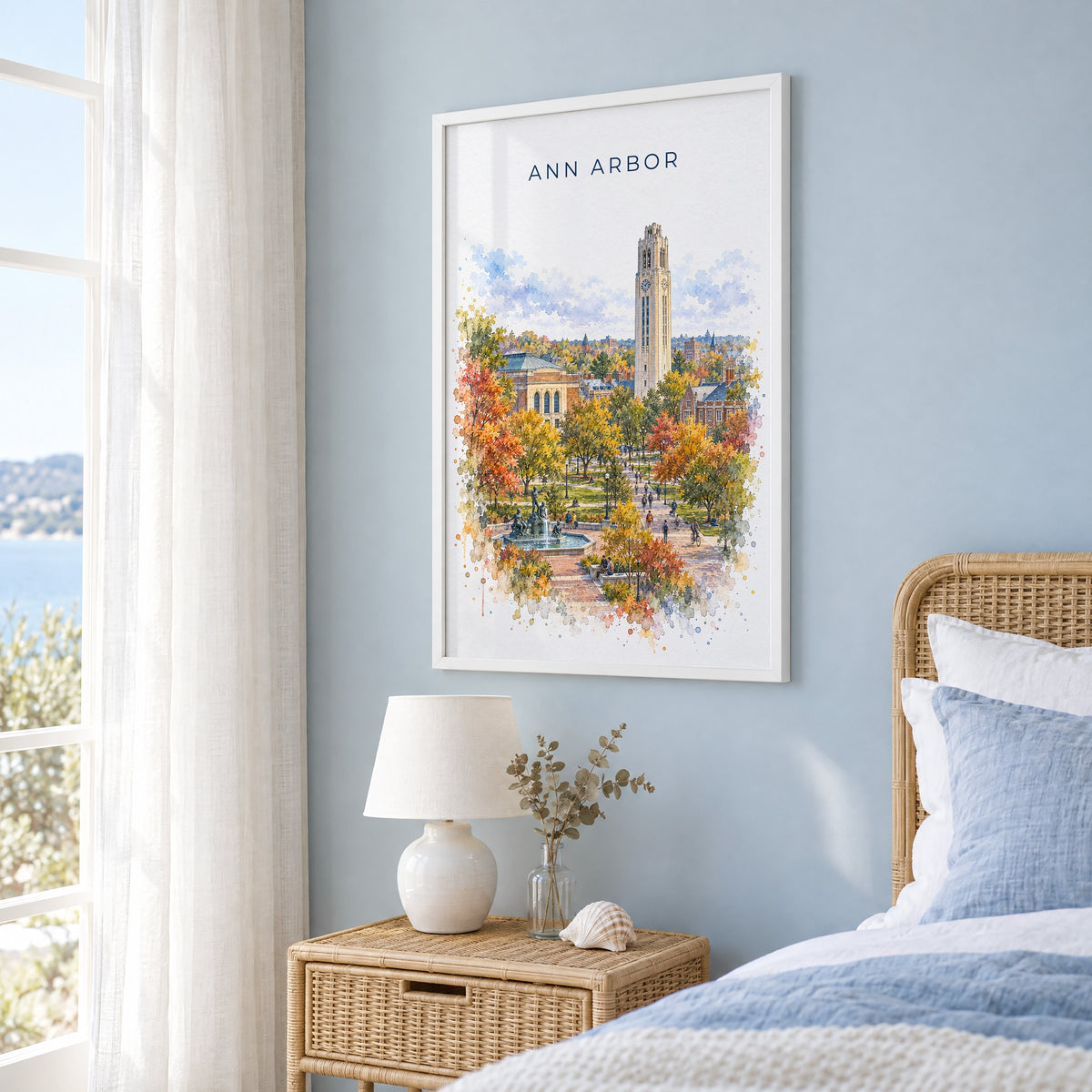 Ann Arbor watercolor print in a white frame on a pale blue wall beside a rattan bed in a coastal bedroom