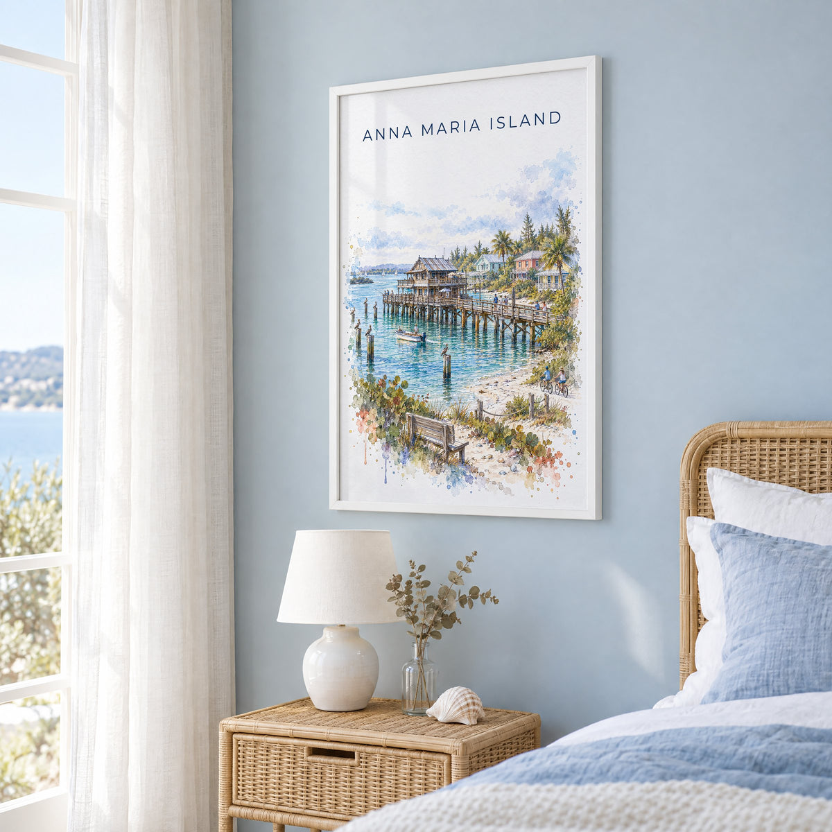 Anna Maria Island watercolor print in a white frame on a pale blue wall beside a rattan bed in a coastal bedroom