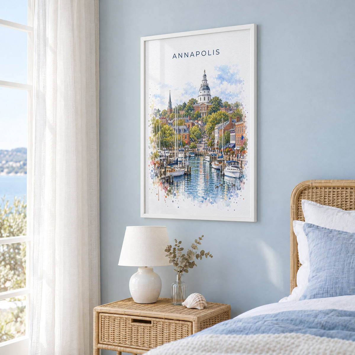 Annapolis watercolor print in a white frame on a pale blue wall beside a rattan bed in a coastal bedroom