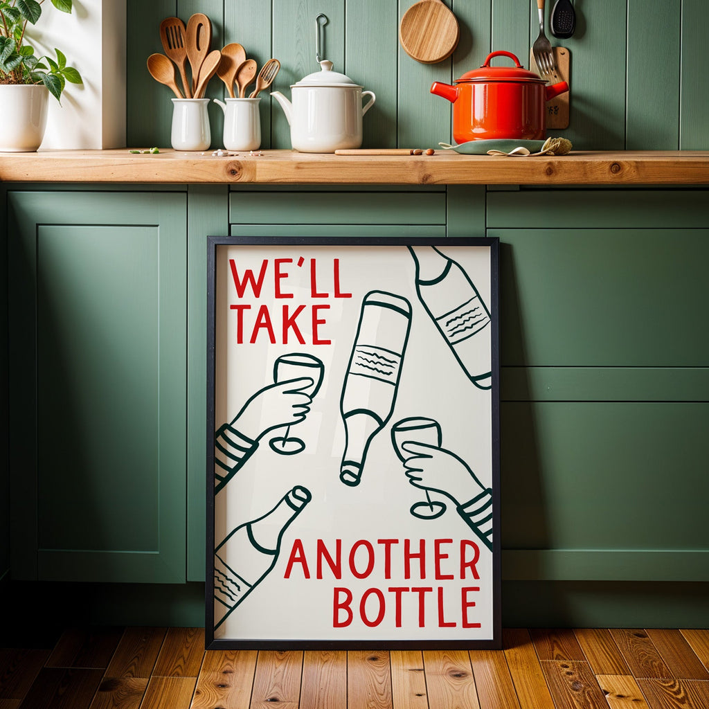 We'll Take Another Bottle wine print in a black frame against sage green kitchen cabinets