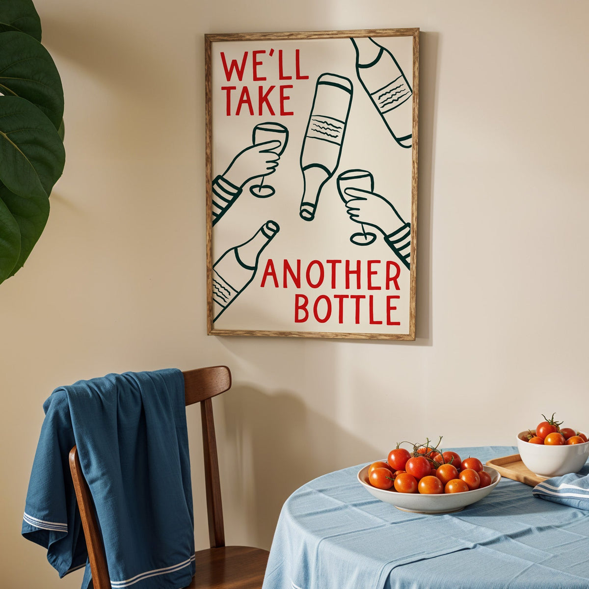 We'll Take Another Bottle wine print in an oak frame above a blue linen table with ripe tomatoes