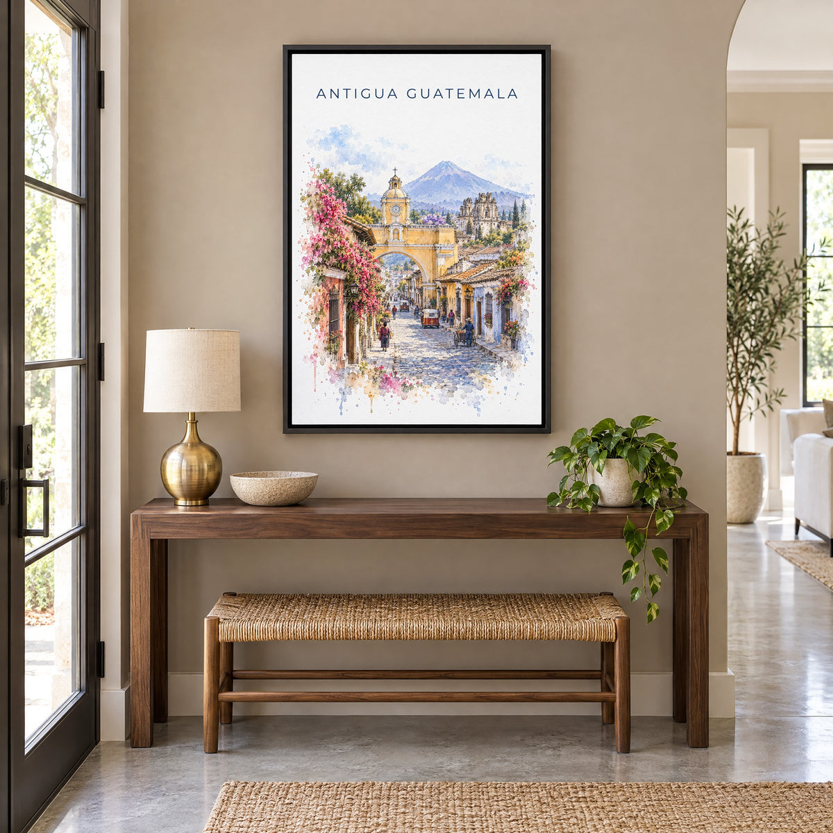 Antigua Guatemala watercolor print as a black floater canvas above a walnut console and woven bench in an entryway