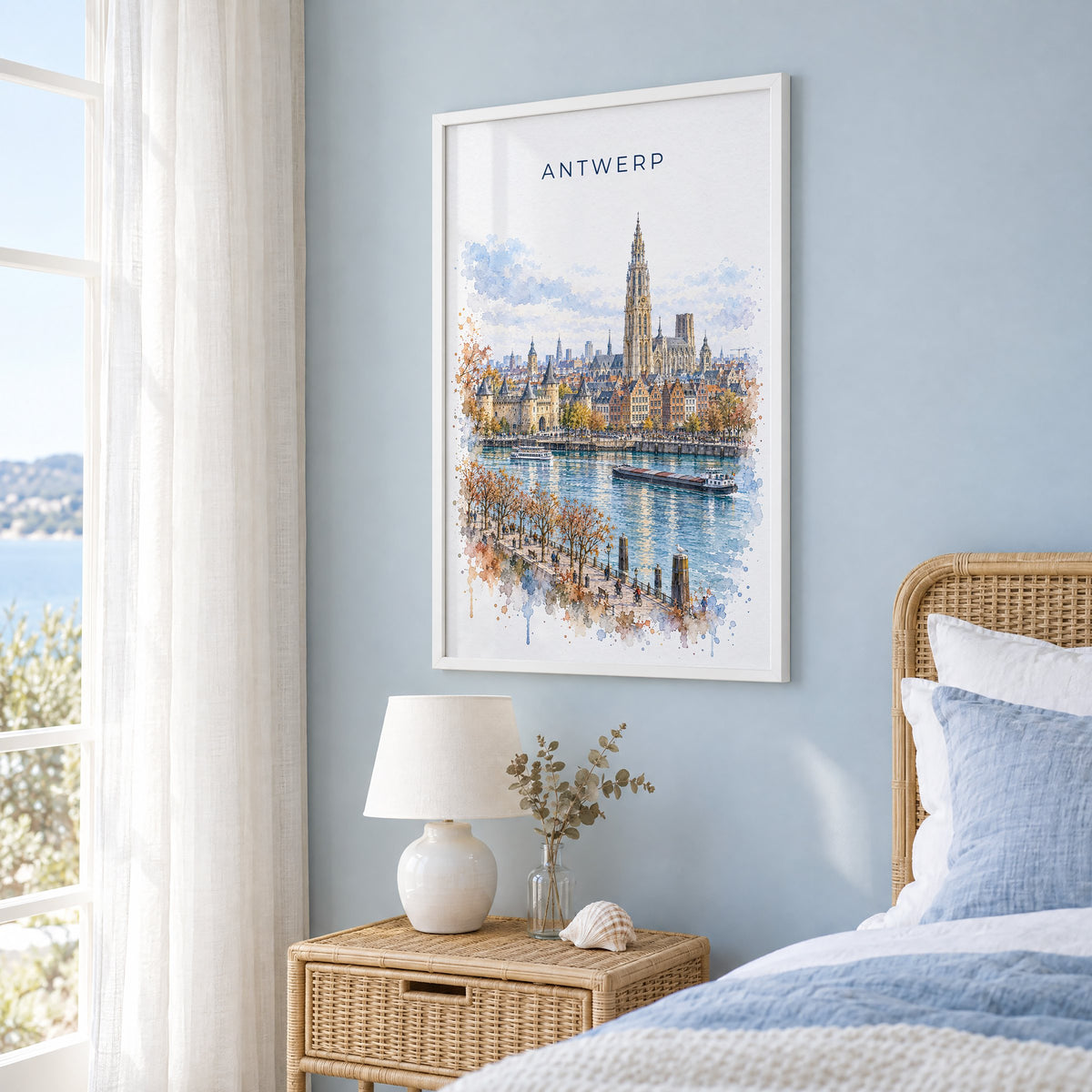 Antwerp watercolor print in a white frame on a pale blue wall beside a rattan bed in a coastal bedroom