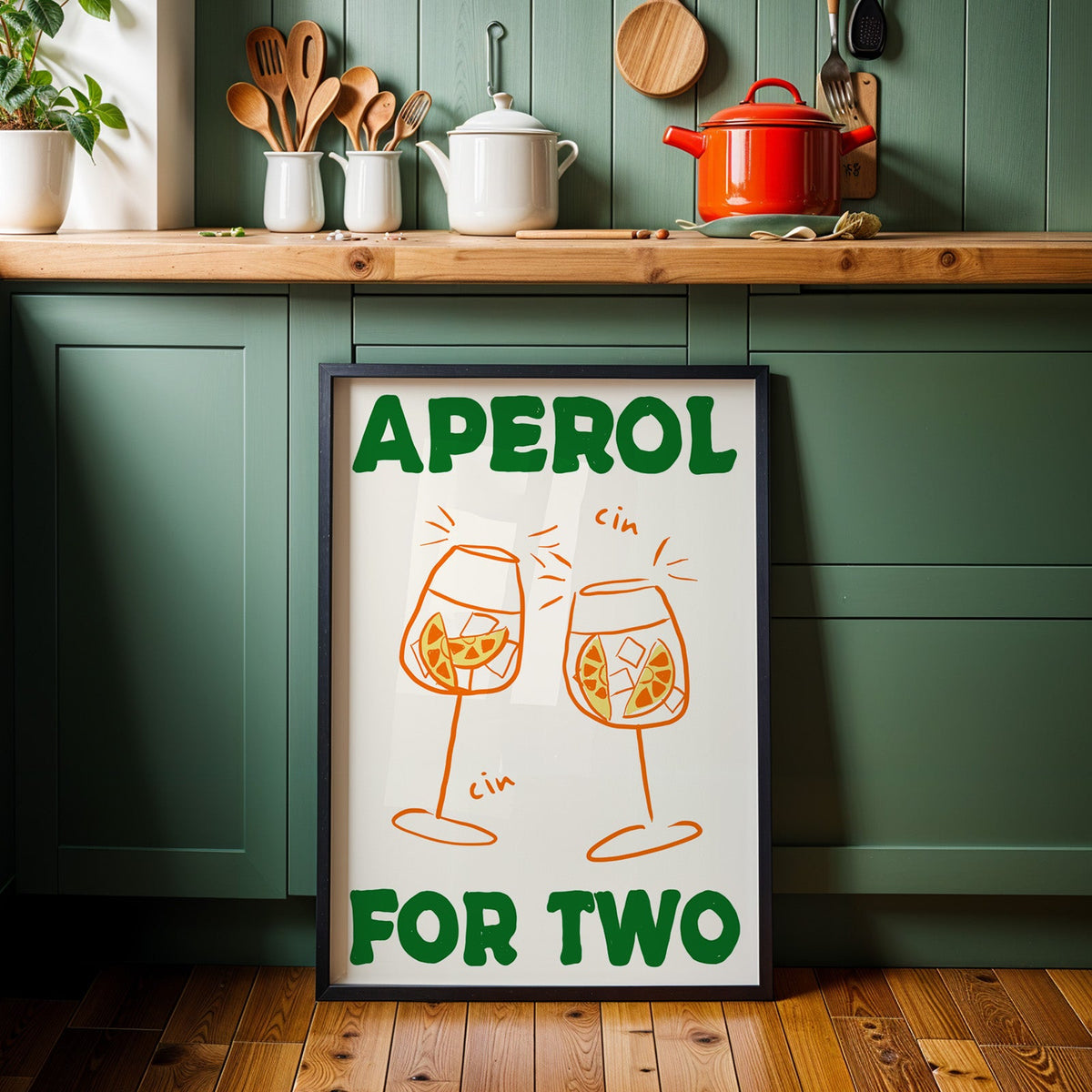 Aperol spritz print in a black frame against sage green kitchen cabinets