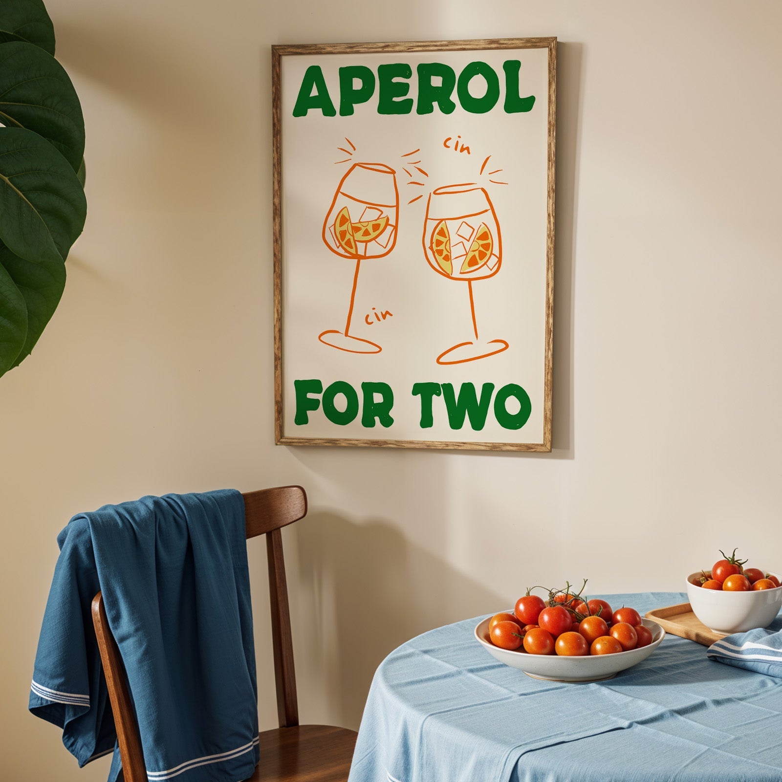 Aperol spritz print in an oak frame above a blue linen table with ripe tomatoes