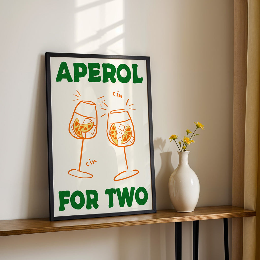 Aperol spritz print in a black frame on a console table with yellow daisies