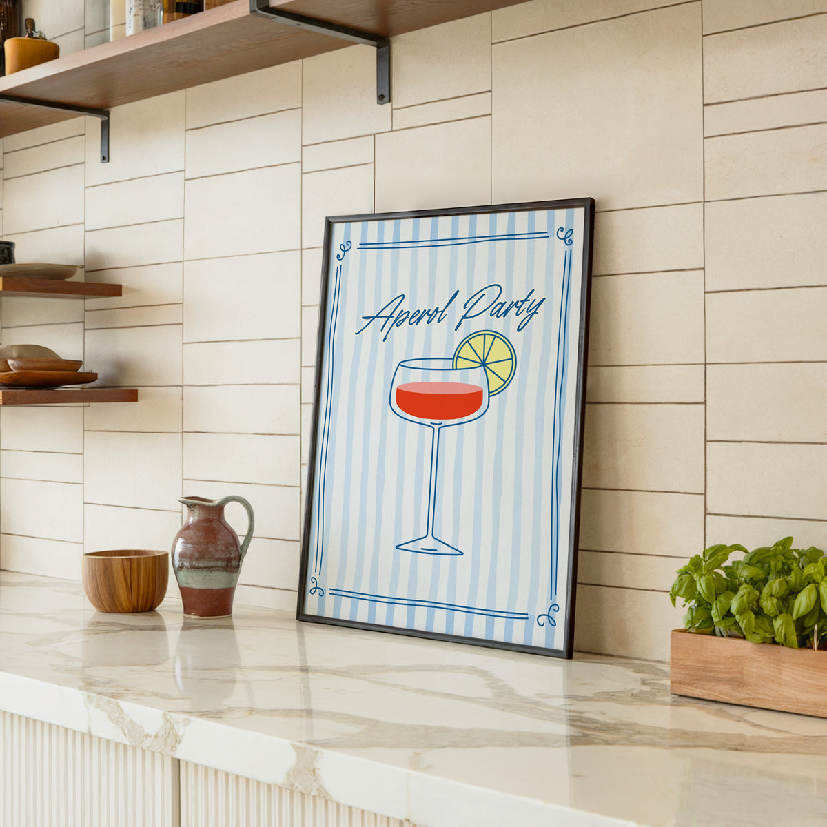 Aperol Party print in a black frame leaning on a marble counter in a tiled kitchen