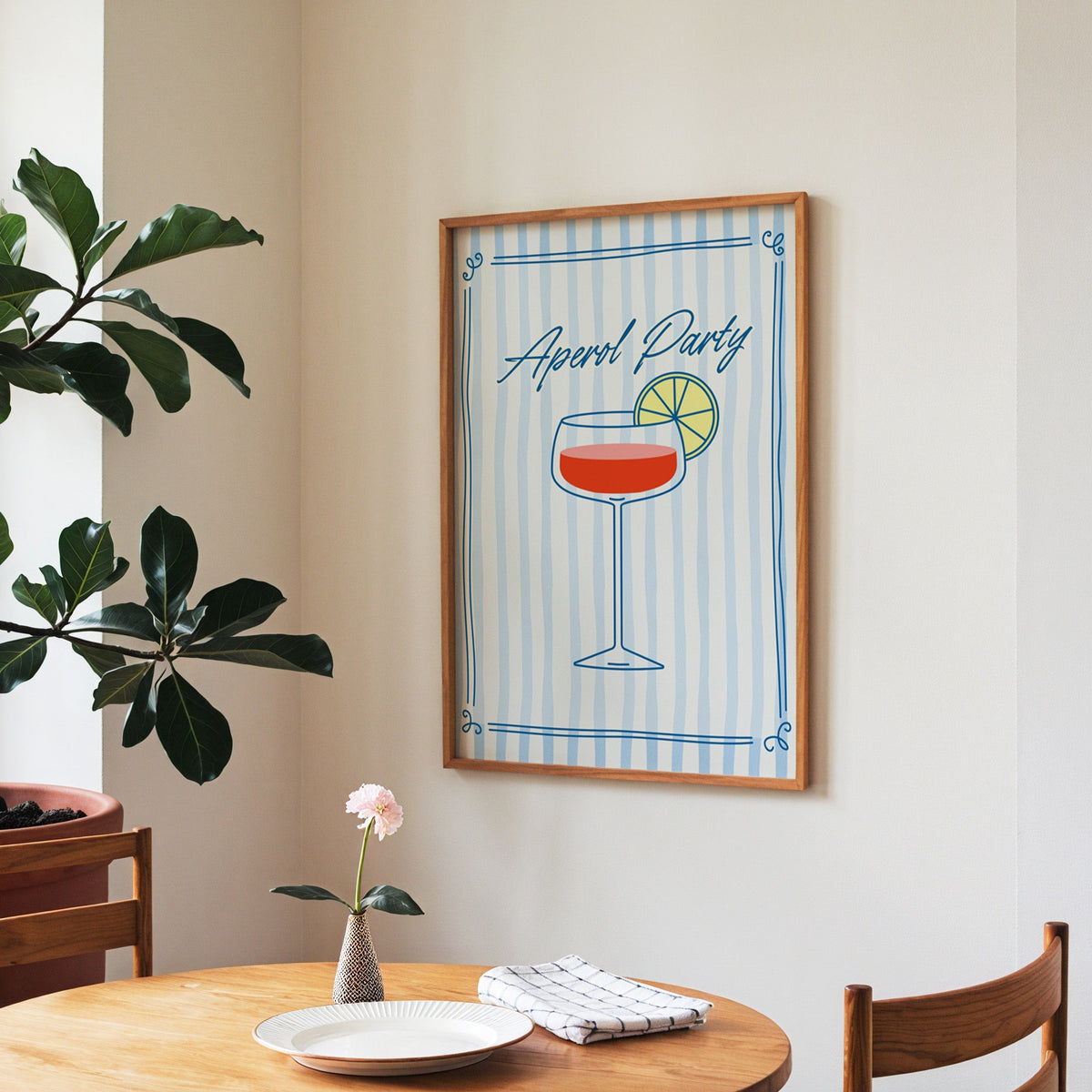 Aperol Party print in a walnut frame above a round table beside a fiddle-leaf fig