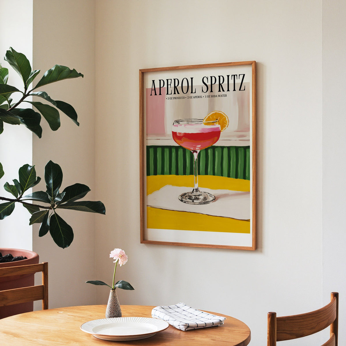 Aperol Spritz recipe print in a walnut frame above a round table beside a fiddle-leaf fig