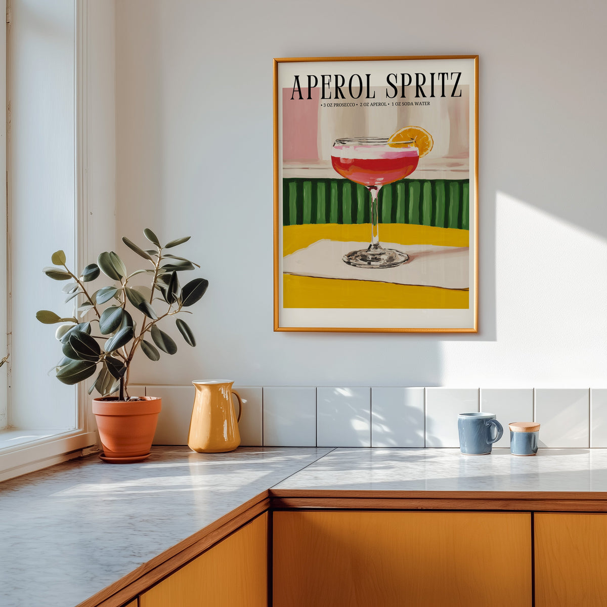 Aperol Spritz recipe print shown in a gold frame above a marble counter in a tan kitchen