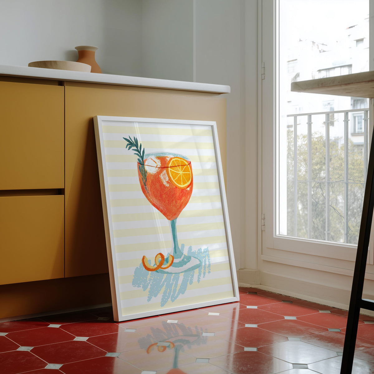 Aperol spritz print in a white frame against yellow cabinets on a red tiled floor