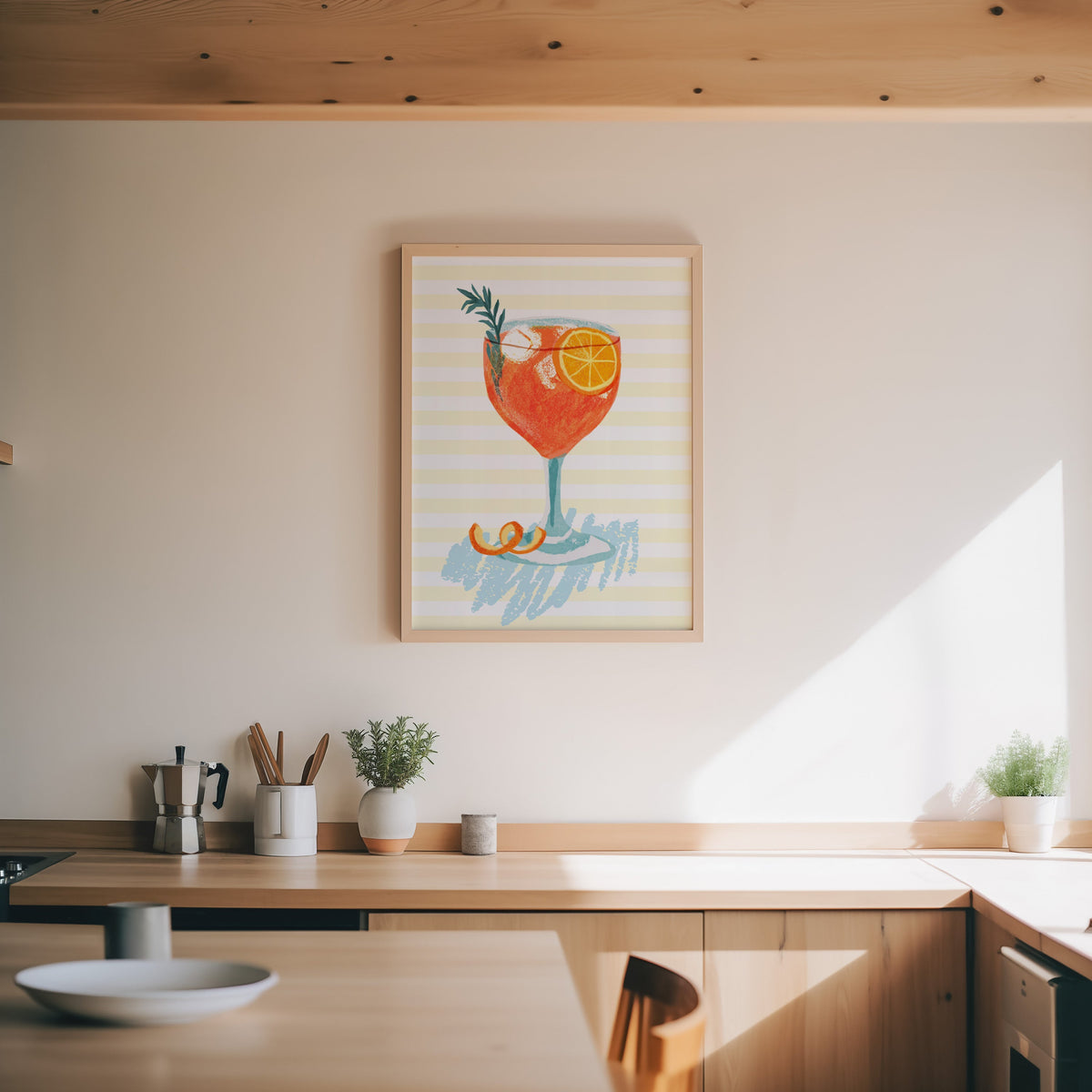 Aperol spritz print in an oak frame above a wood counter with a moka pot and herbs