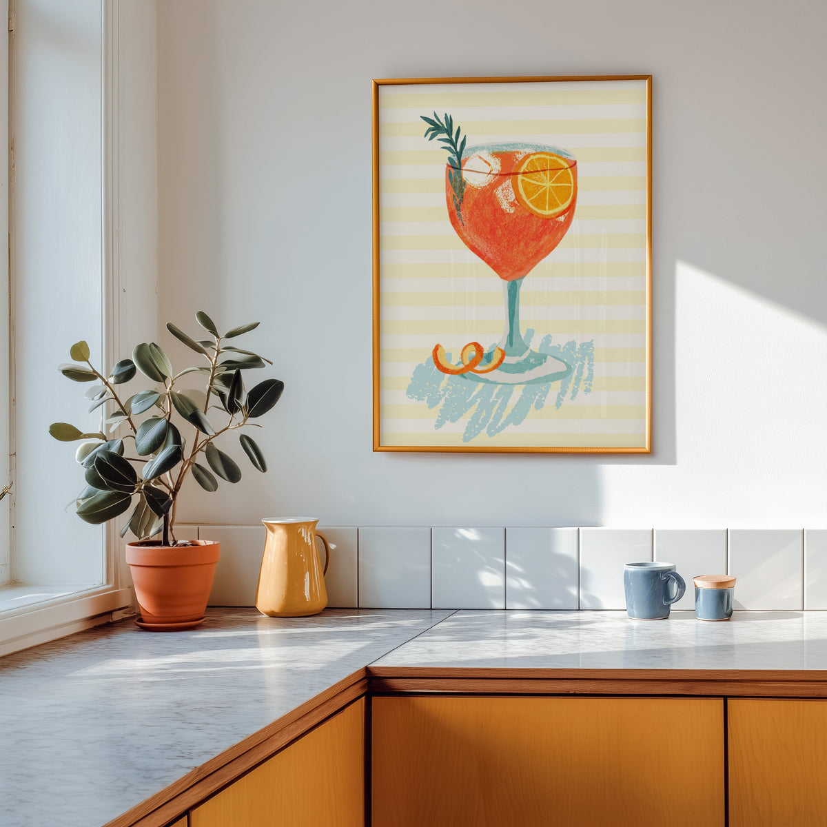 Aperol spritz print shown in a gold frame above a marble counter with a yellow ceramic jug