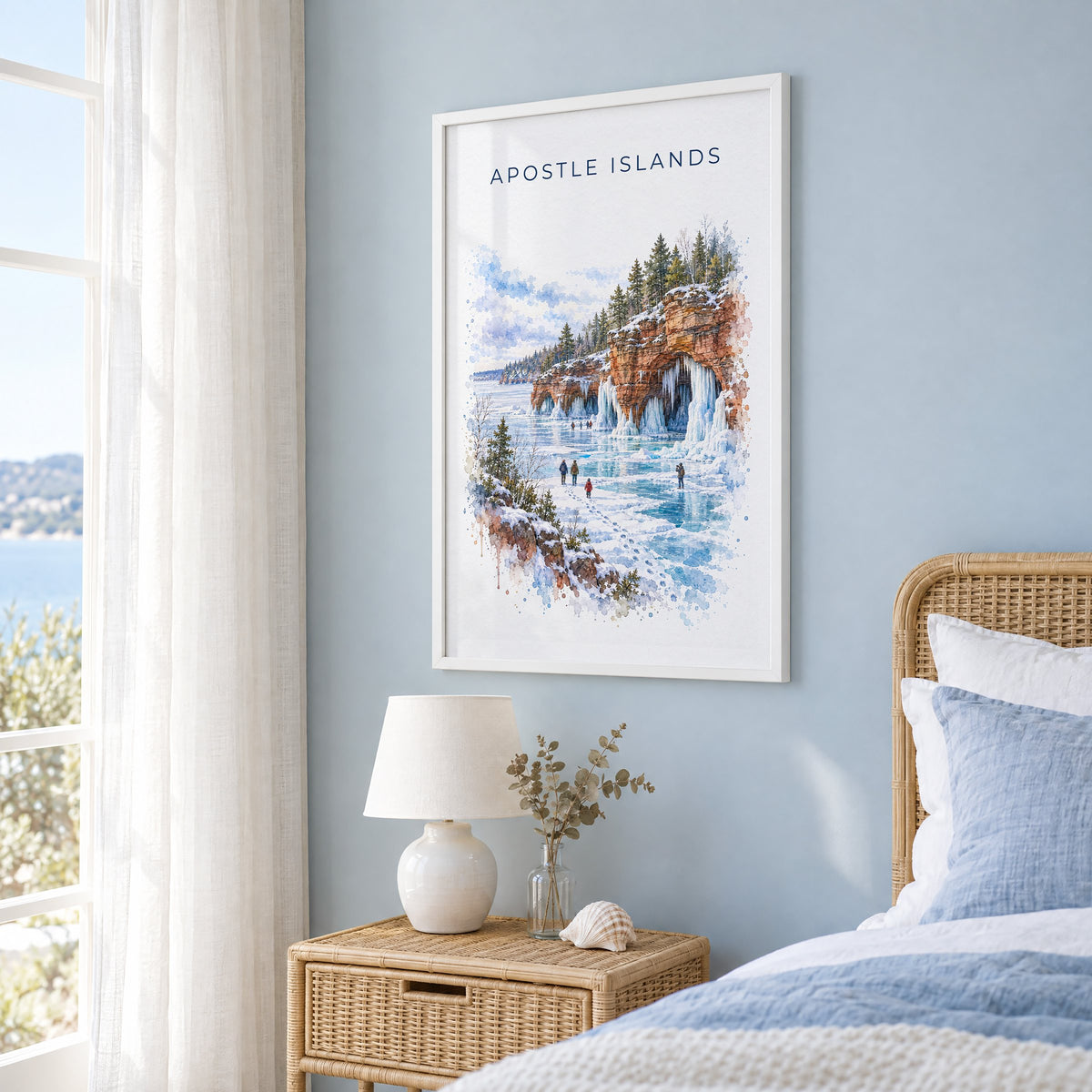 Apostle Islands watercolor print in a white frame on a pale blue wall beside a rattan bed in a coastal bedroom