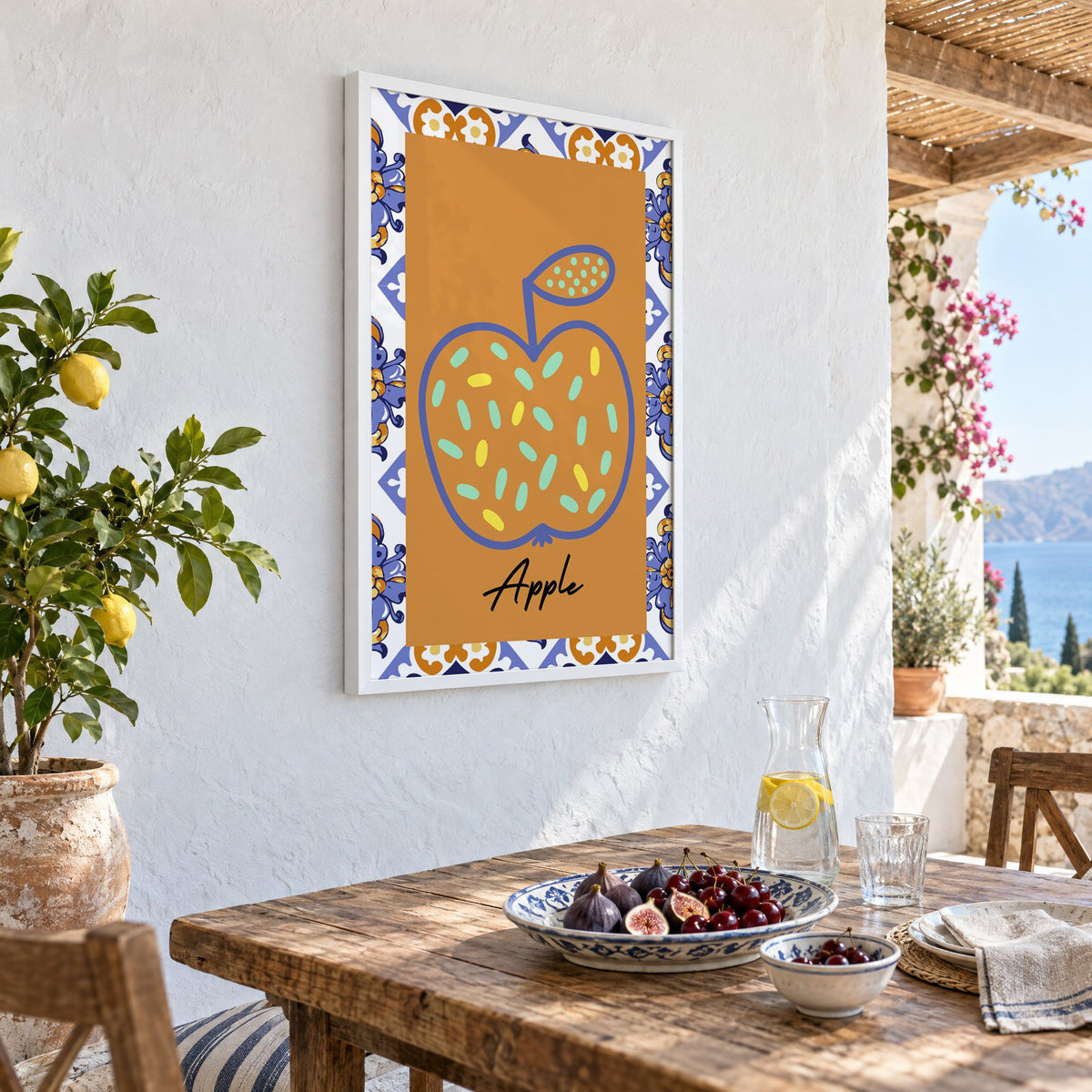 Apple blue outline ochre majolica print in a white frame on a whitewashed terrace wall above a lunch table with figs and cherries, seen at an angle