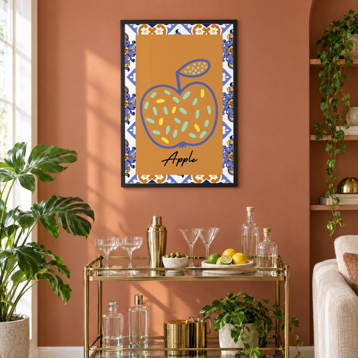 Apple blue outline ochre majolica print in a black frame on a terracotta wall above a brass bar cart with coupes and citrus