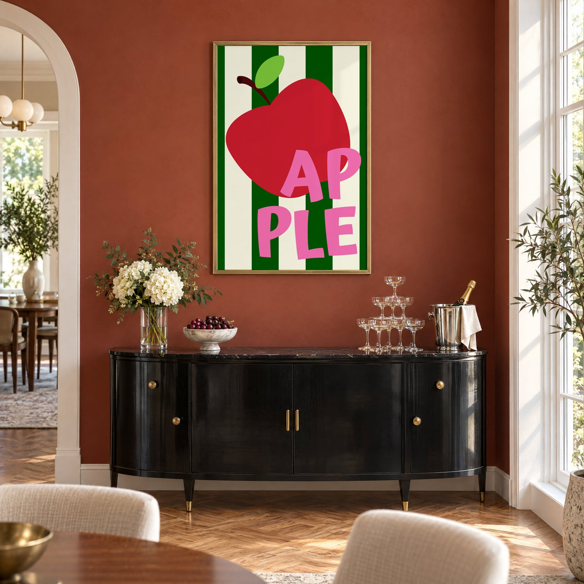 AP PLE red apple stripes print in a brass frame on a terracotta wall above a black buffet with a champagne tower