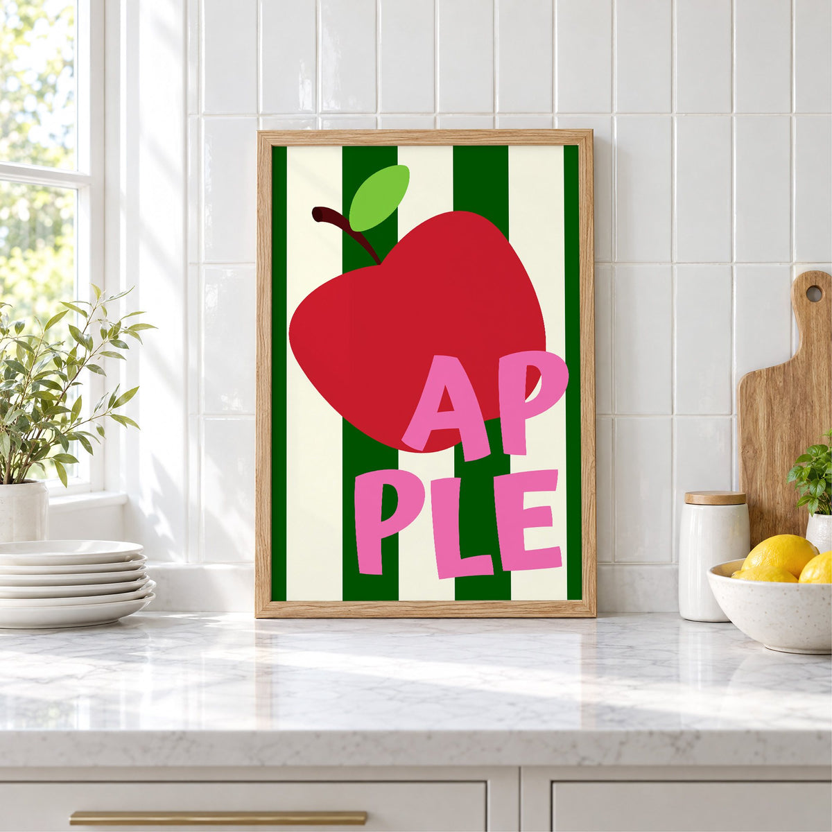 AP PLE red apple stripes print in an oak frame leaning on a marble counter by white tiles and lemons