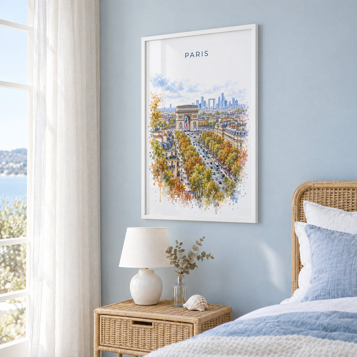 Arc de Triomphe watercolor print in a white frame on a pale blue wall beside a rattan bed in a coastal bedroom