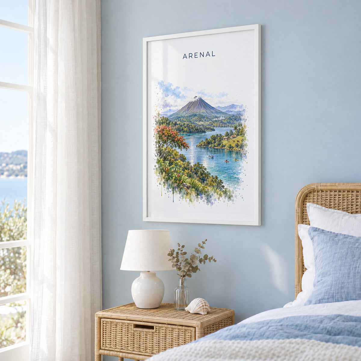 Arenal Volcano watercolor print in a white frame on a pale blue wall beside a rattan bed in a coastal bedroom