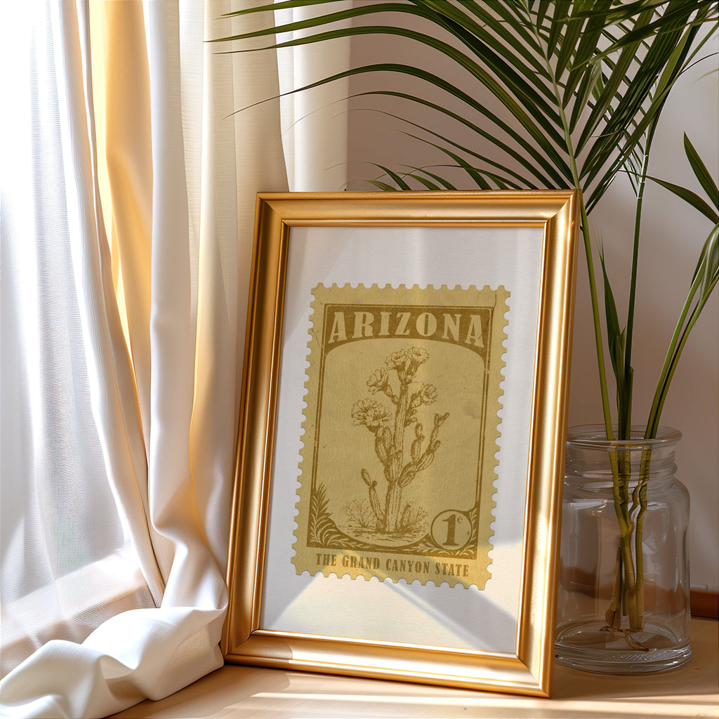 Arizona stamp print in a gold frame leaning by a cream curtain with a palm in a glass jar