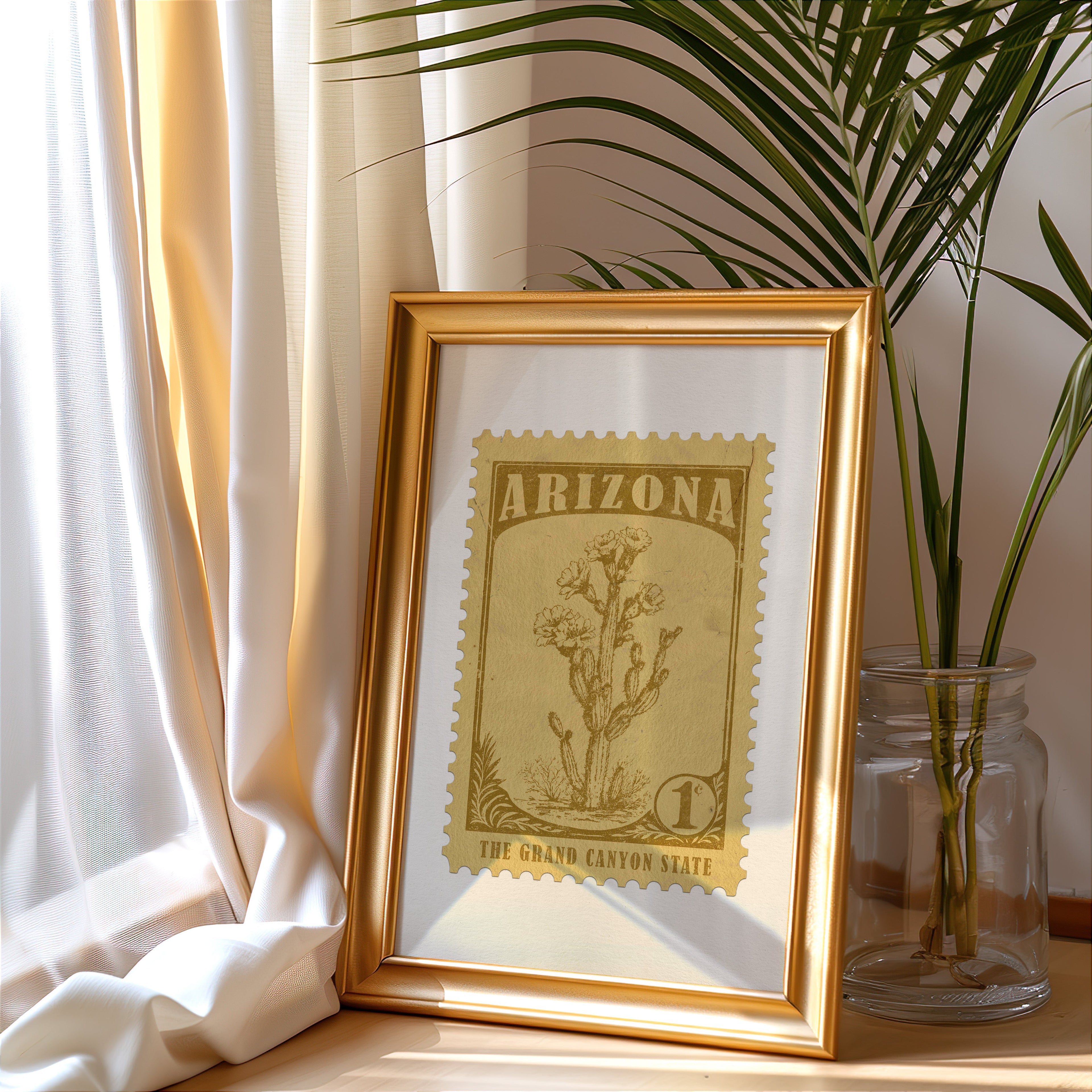 Arizona stamp print in a gold frame leaning by a cream curtain with a palm in a glass jar
