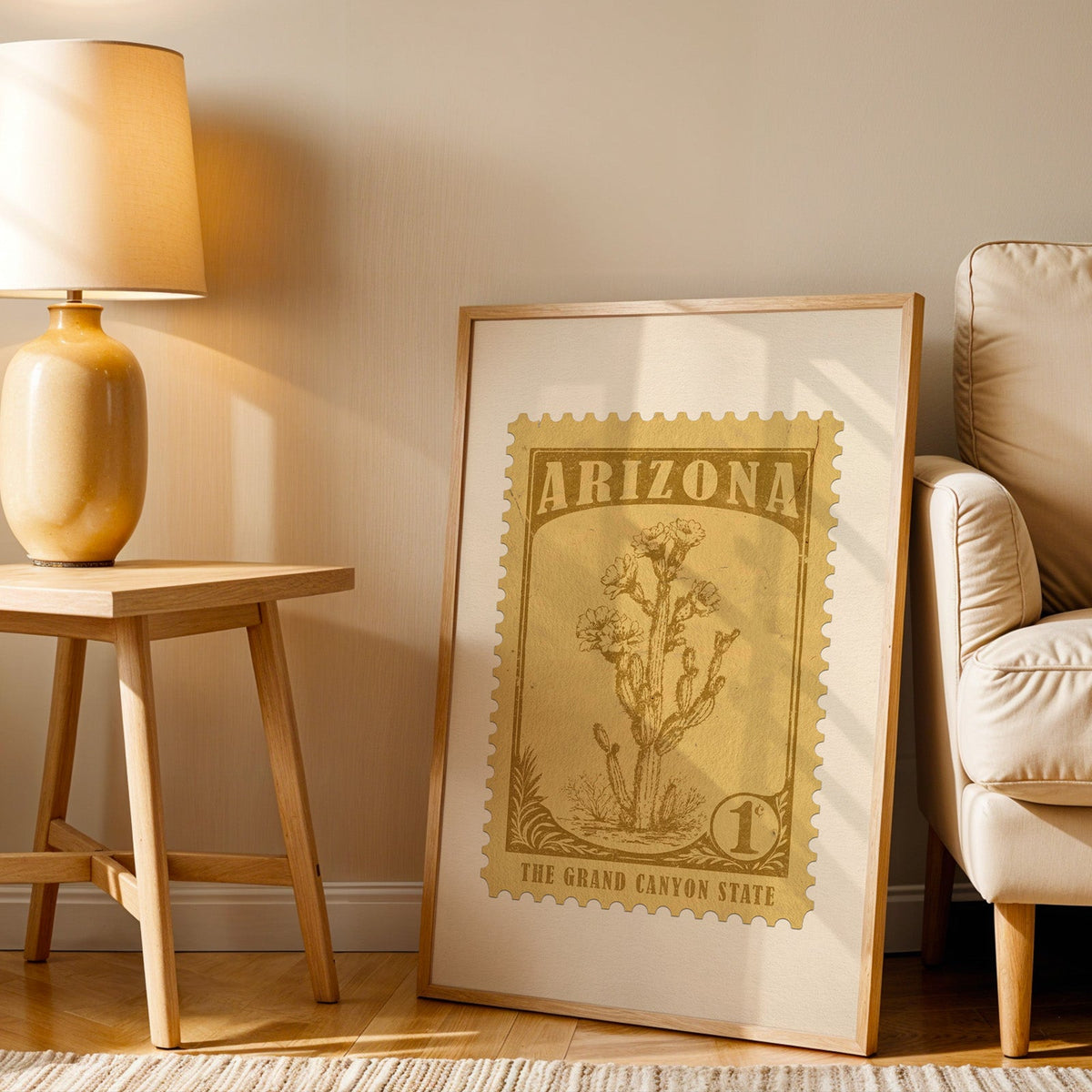 Arizona stamp print in a wood frame resting on the floor beside a beige armchair and a yellow table lamp