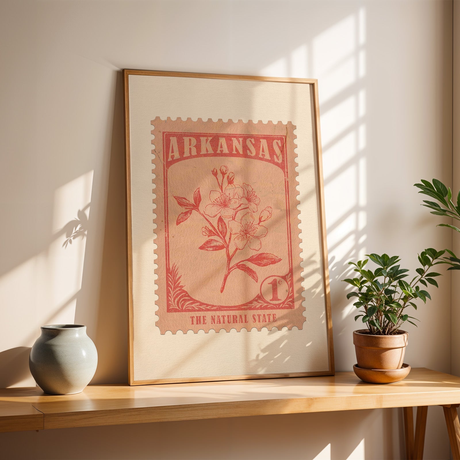 Arkansas apple blossom stamp print in a light oak frame leaning on a wooden table beside a stoneware vase