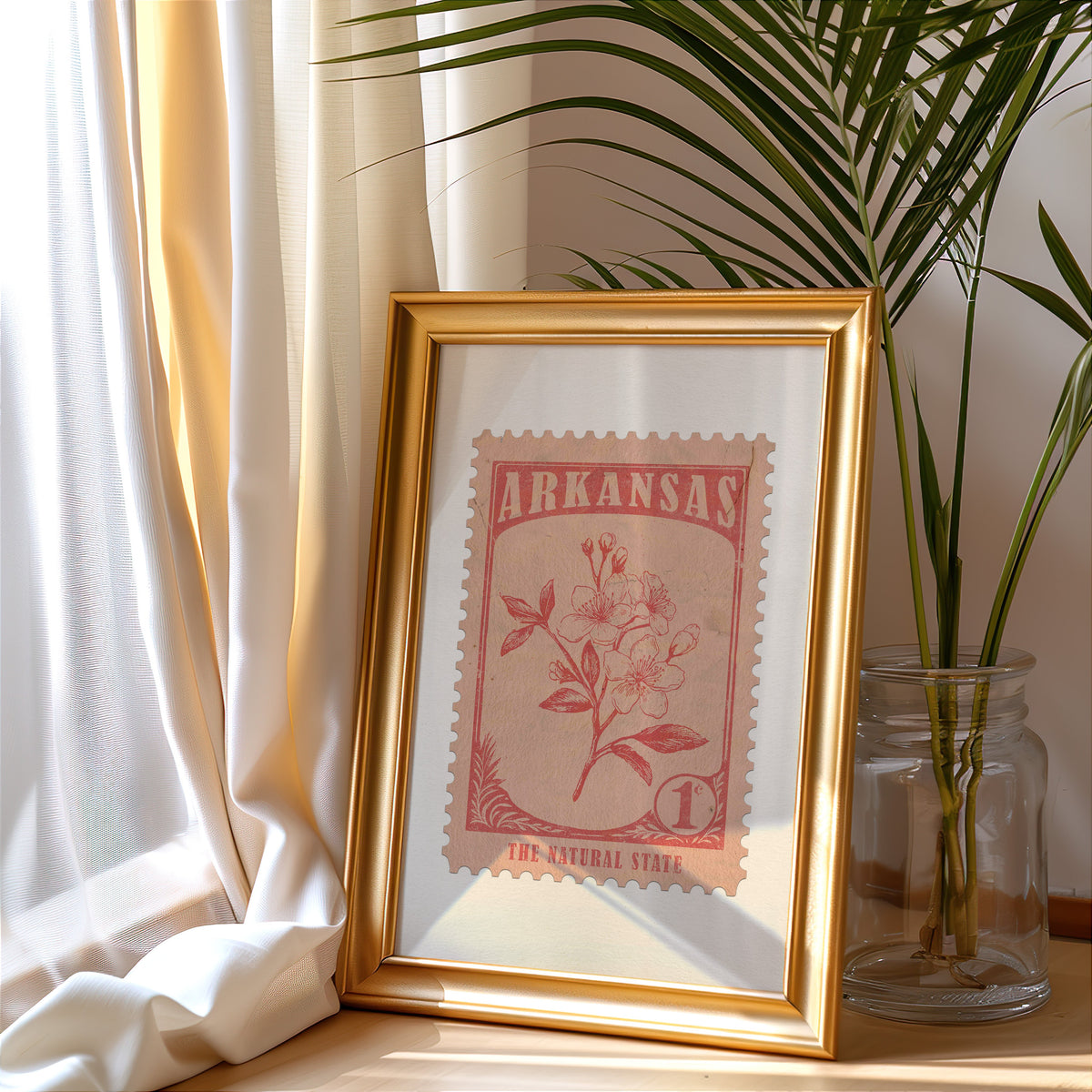 Arkansas stamp print in a gold frame leaning by a cream curtain with a palm in a glass jar