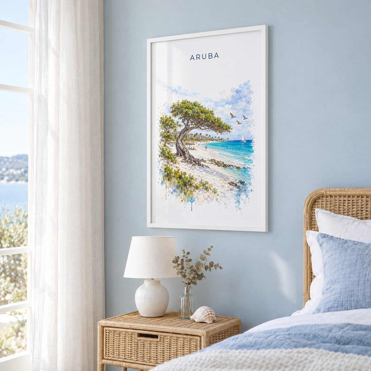 Aruba watercolor print in a white frame on a pale blue wall beside a rattan bed in a coastal bedroom
