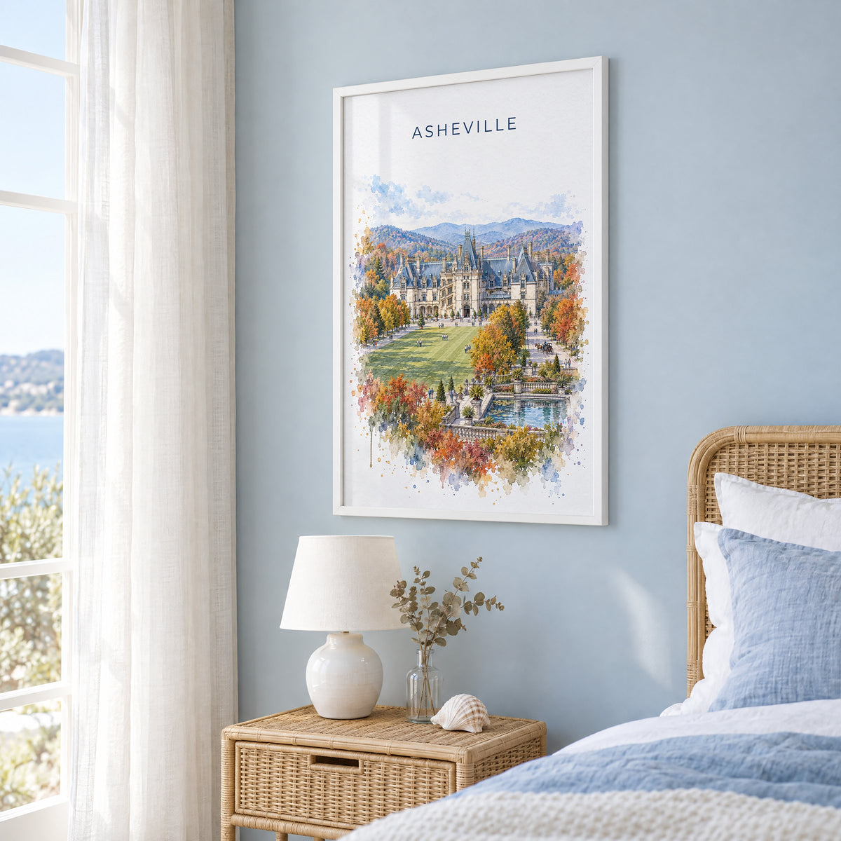Asheville watercolor print in a white frame on a pale blue wall beside a rattan bed in a coastal bedroom